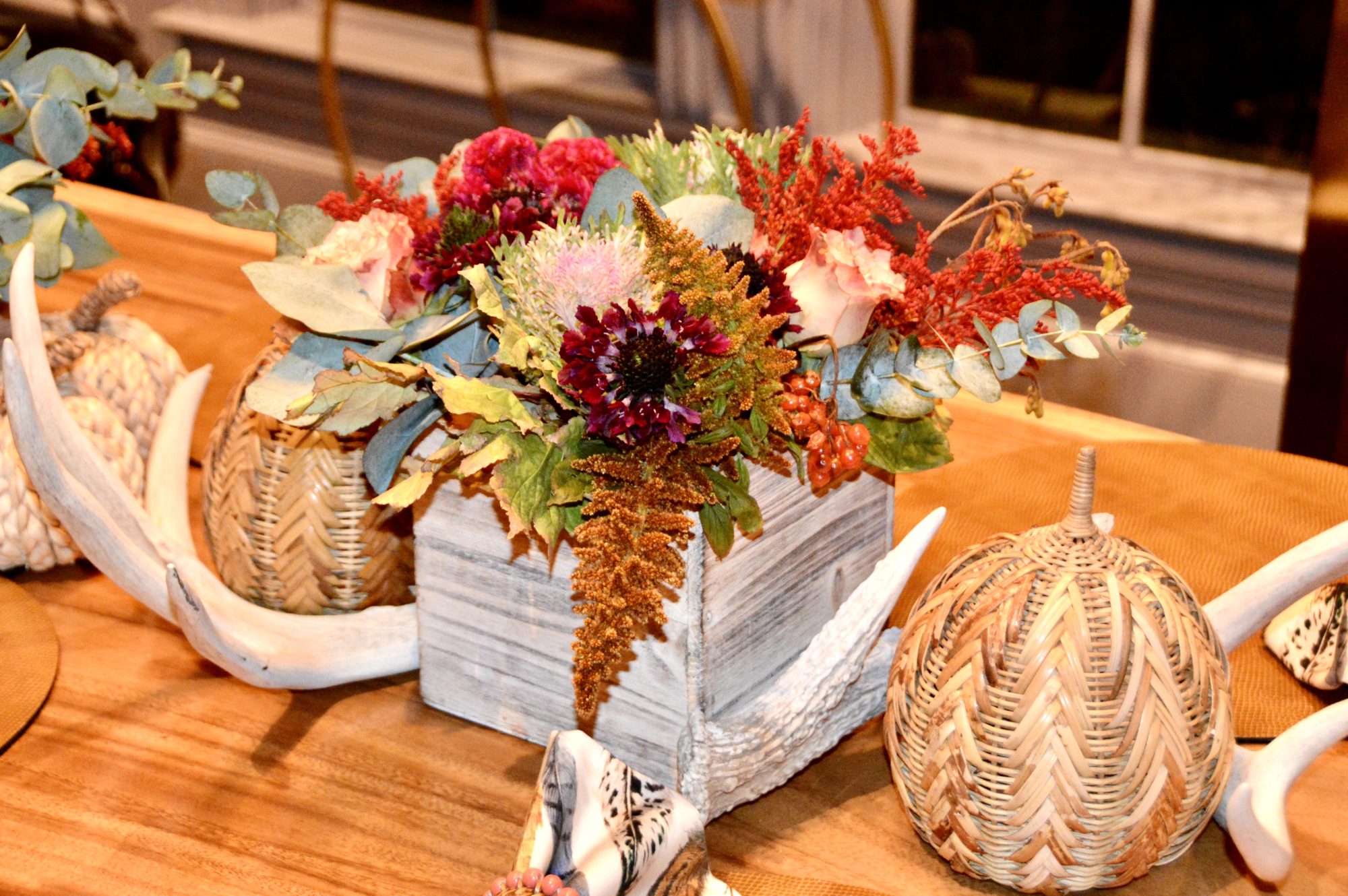 Fall centerpiece of autumn flowers in a white box with pumpkins and antlers on a wood table