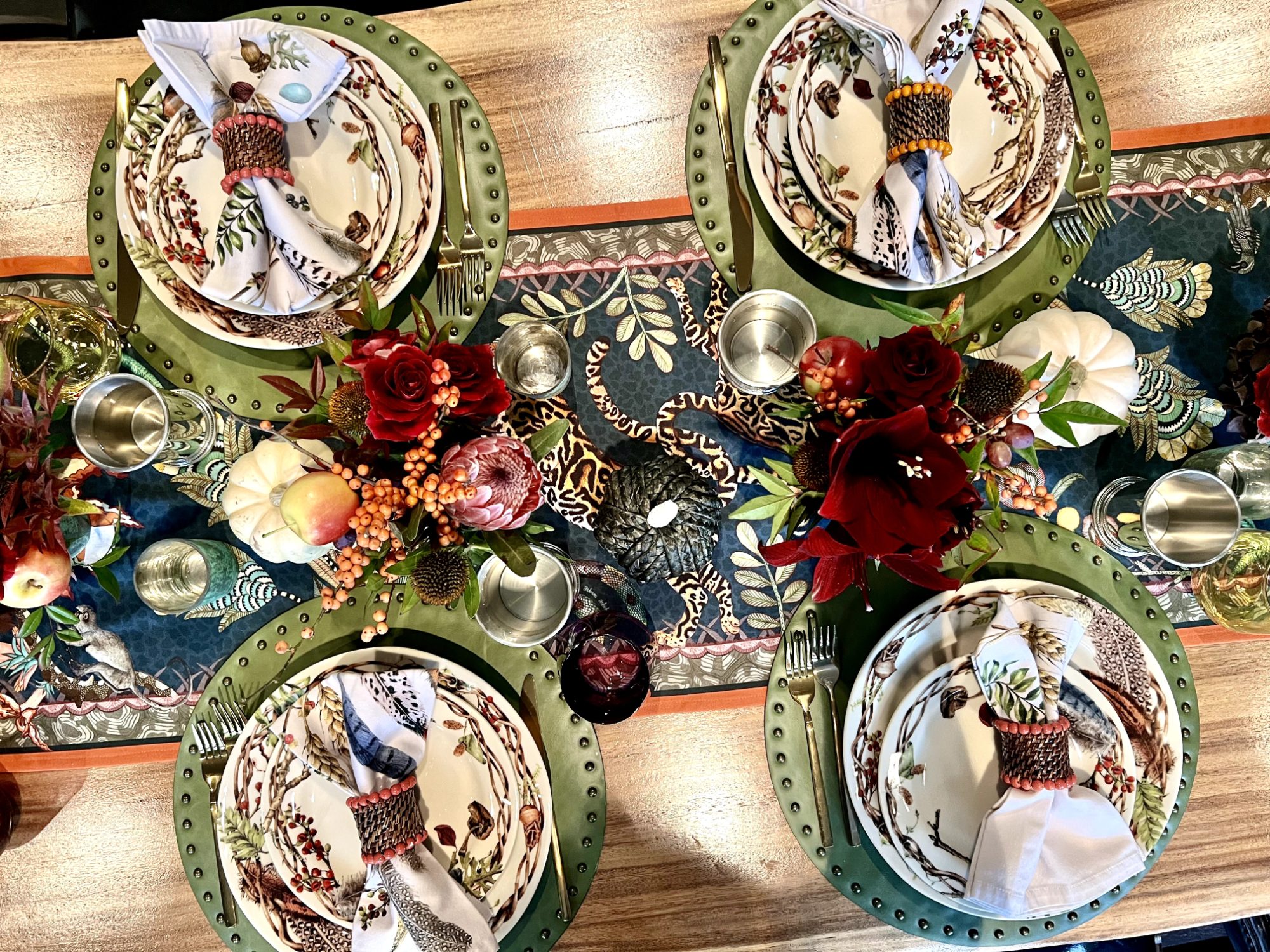 Overhead view of a Thanksgiving table with green chargers, patterned plates and deep red flowers